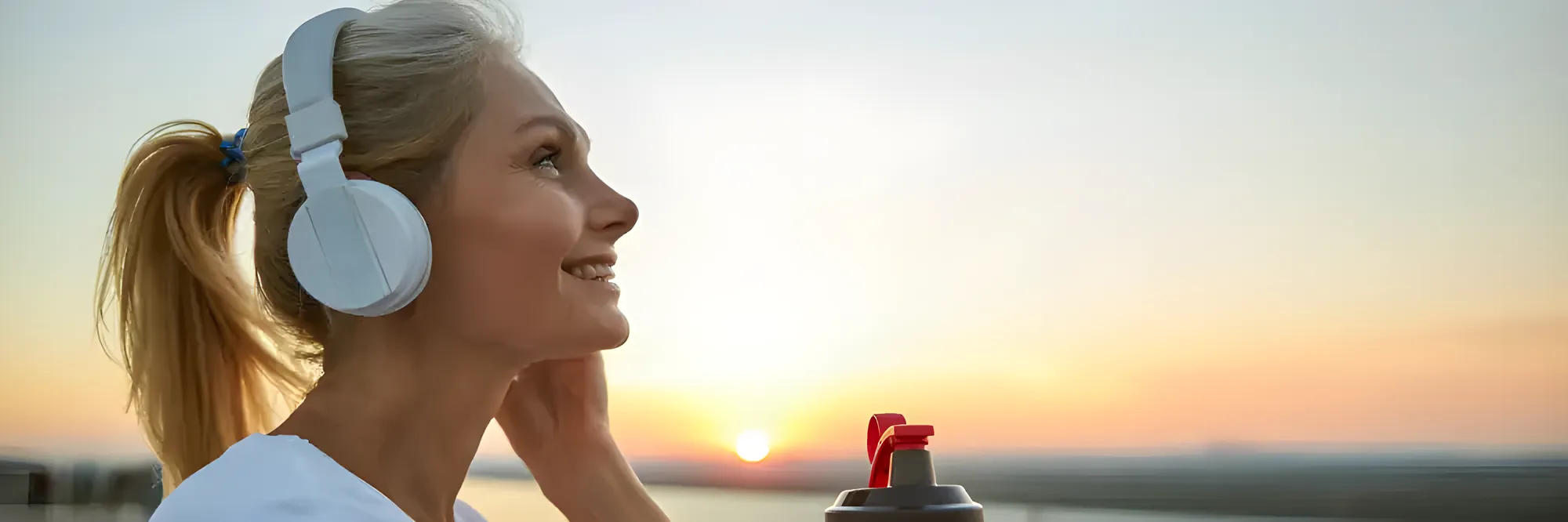 Eine Frau mit Kopfhörern blickt bei Sonnenuntergang in die Ferne